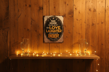 Load image into Gallery viewer, This House Runs Best on Love Laughter and Good Beer metal wall sign in cozy home bar scene